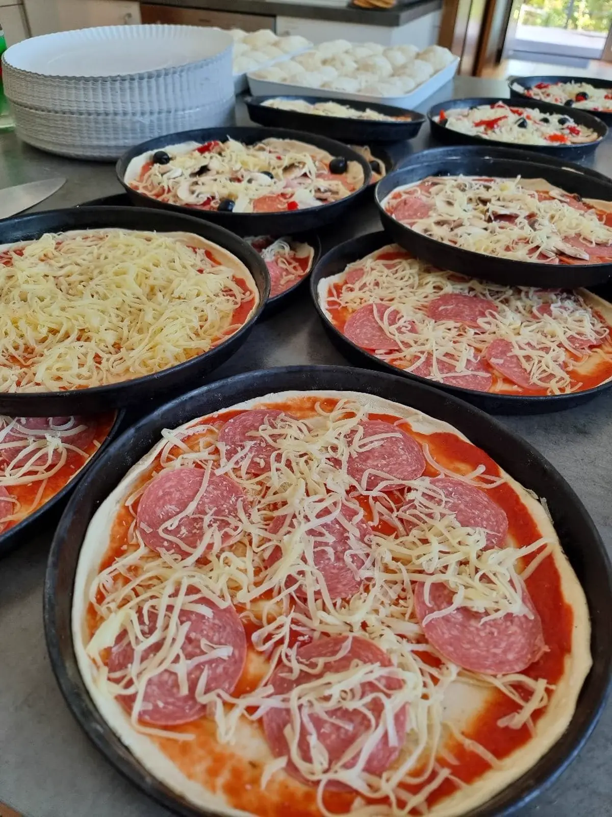 Mehrere Pizzen auf Blechen vor dem Backen
